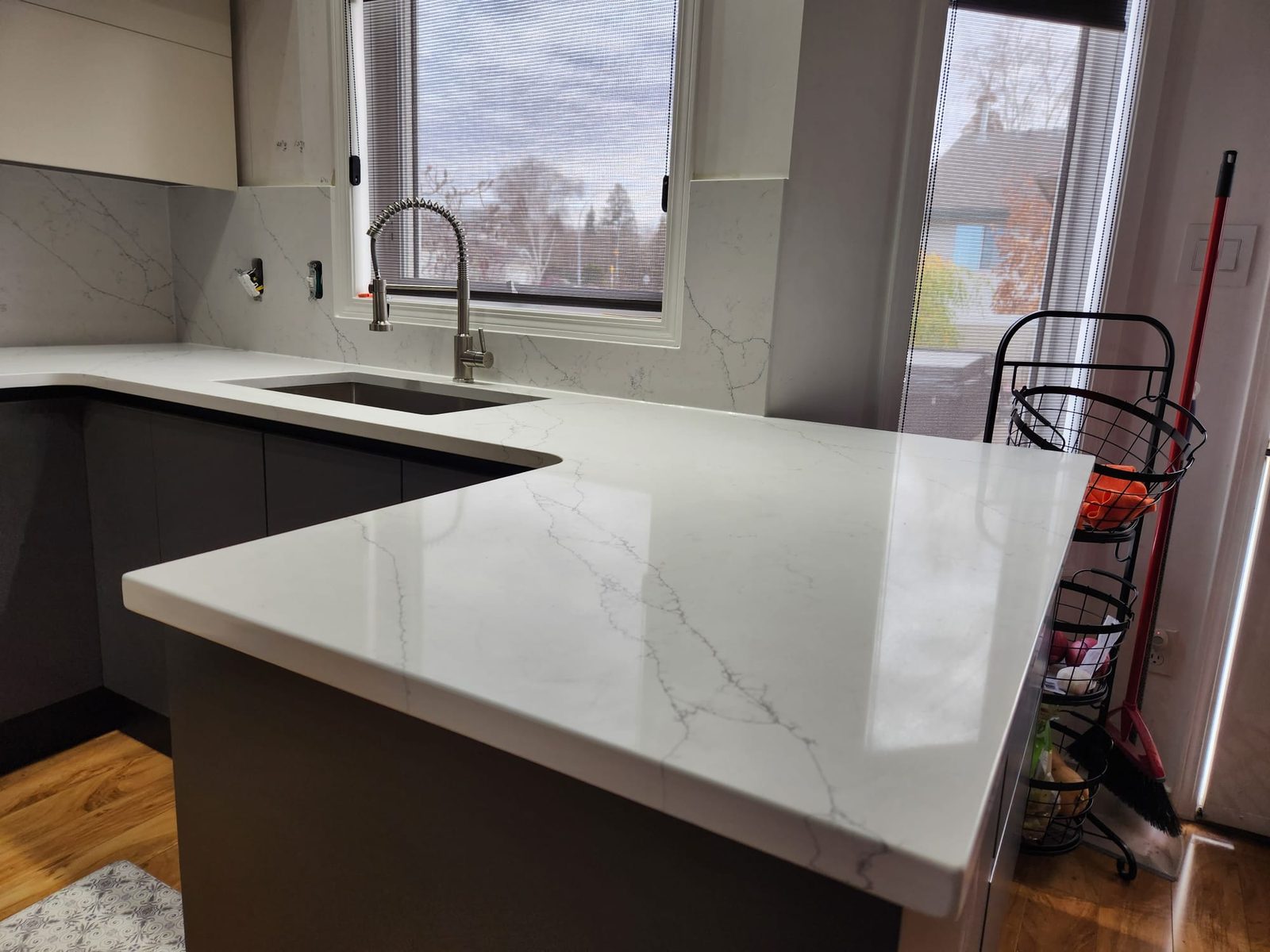 Marble-look quartz counter run along a kitchen window with dark cabinets